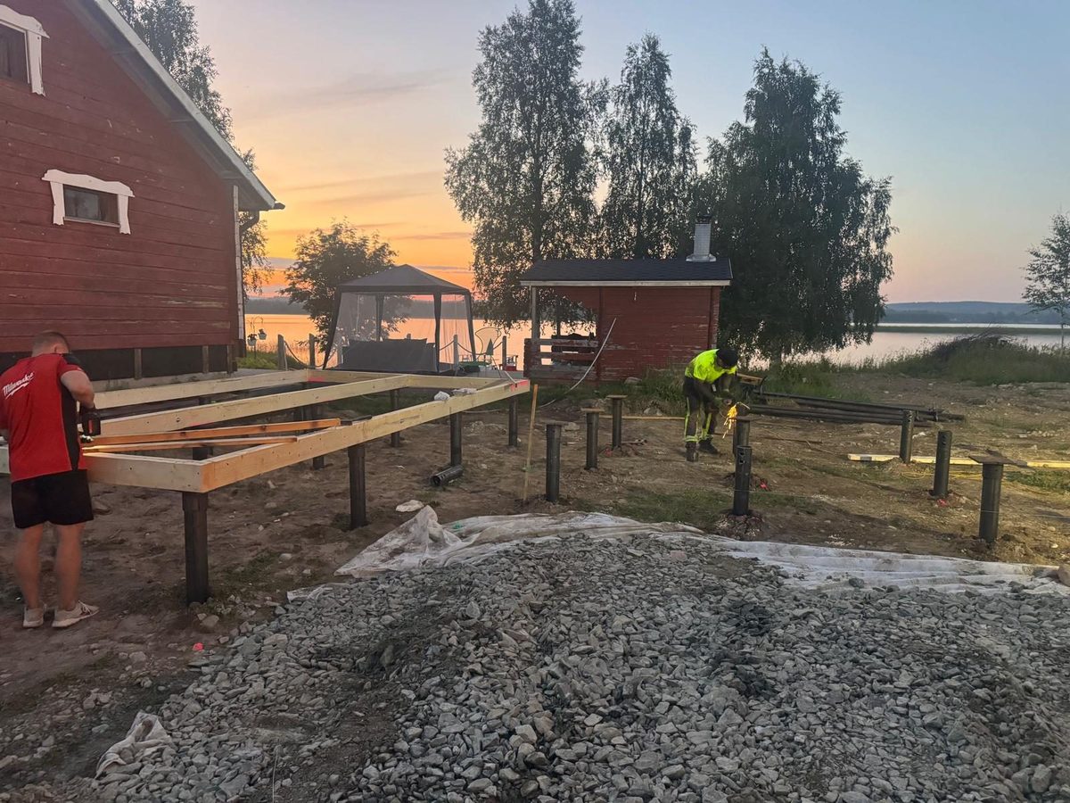 Arbeiter errichten Holzrahmen auf Schraubpfahl-Fundamenten am See